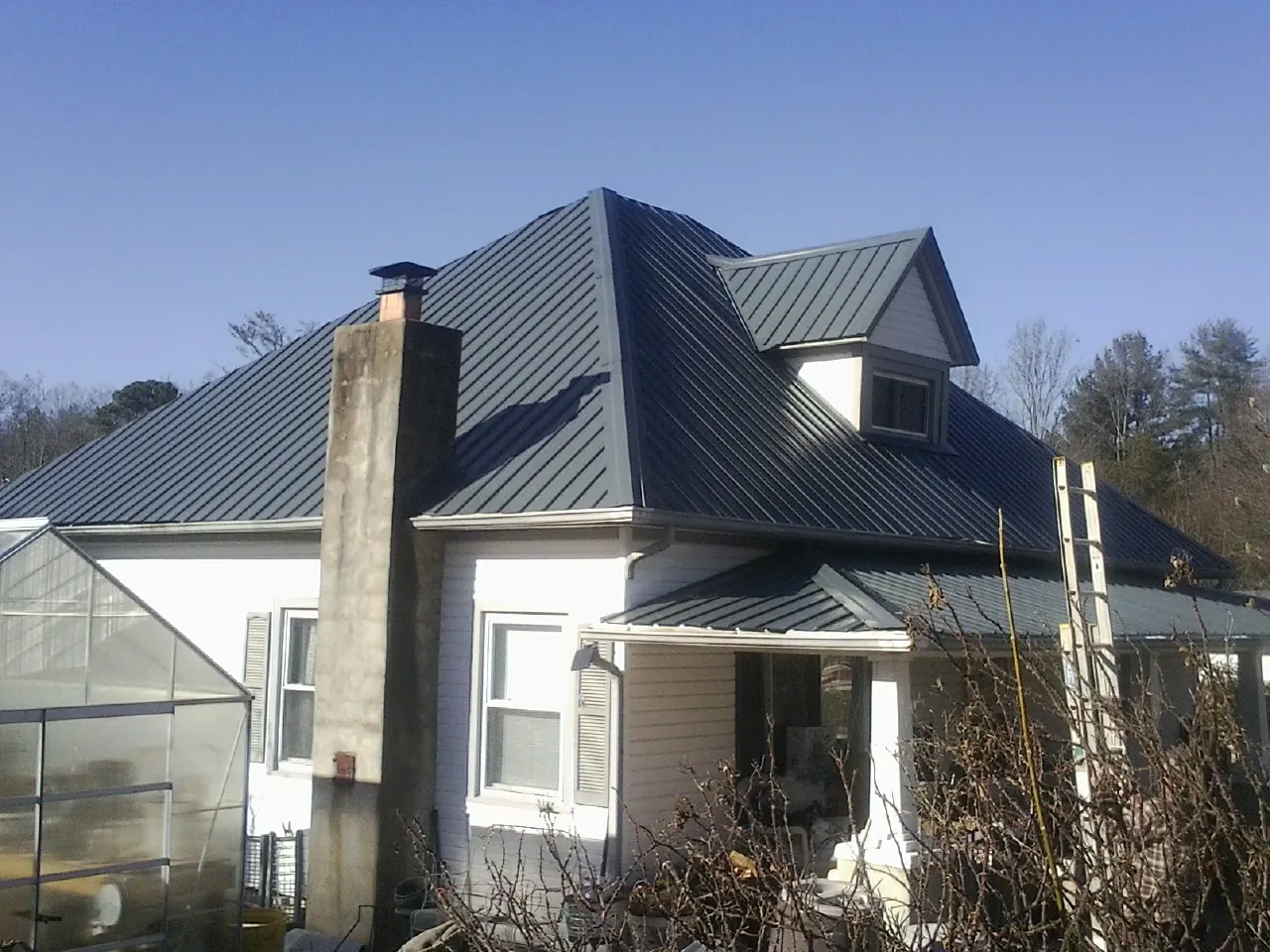 Dark blue standing seam metal roof on a white farmhouse with dormer — Slate & Tile Roof Repair by Roofing Brothers in Manitou