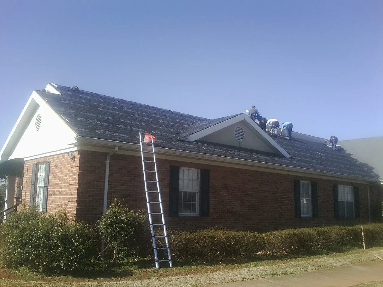 Crew tearing shingles off a brick ranch roof with a ladder set — Emergency Roof Repair work by our crew in Manitou