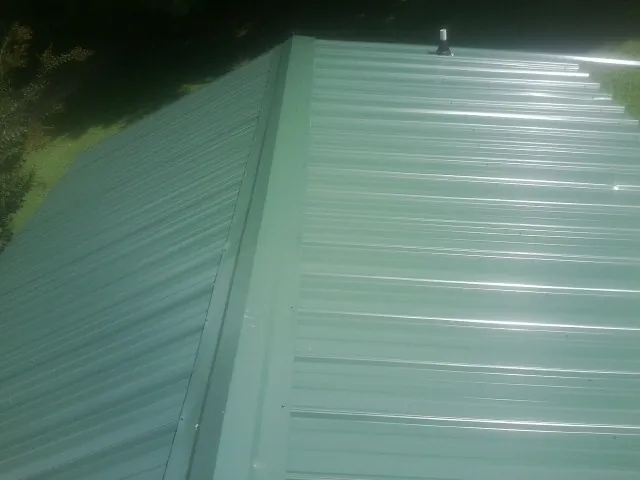 New green metal panels meeting at the ridge of a roof — Flat Roof Repair work by our crew in Manitou