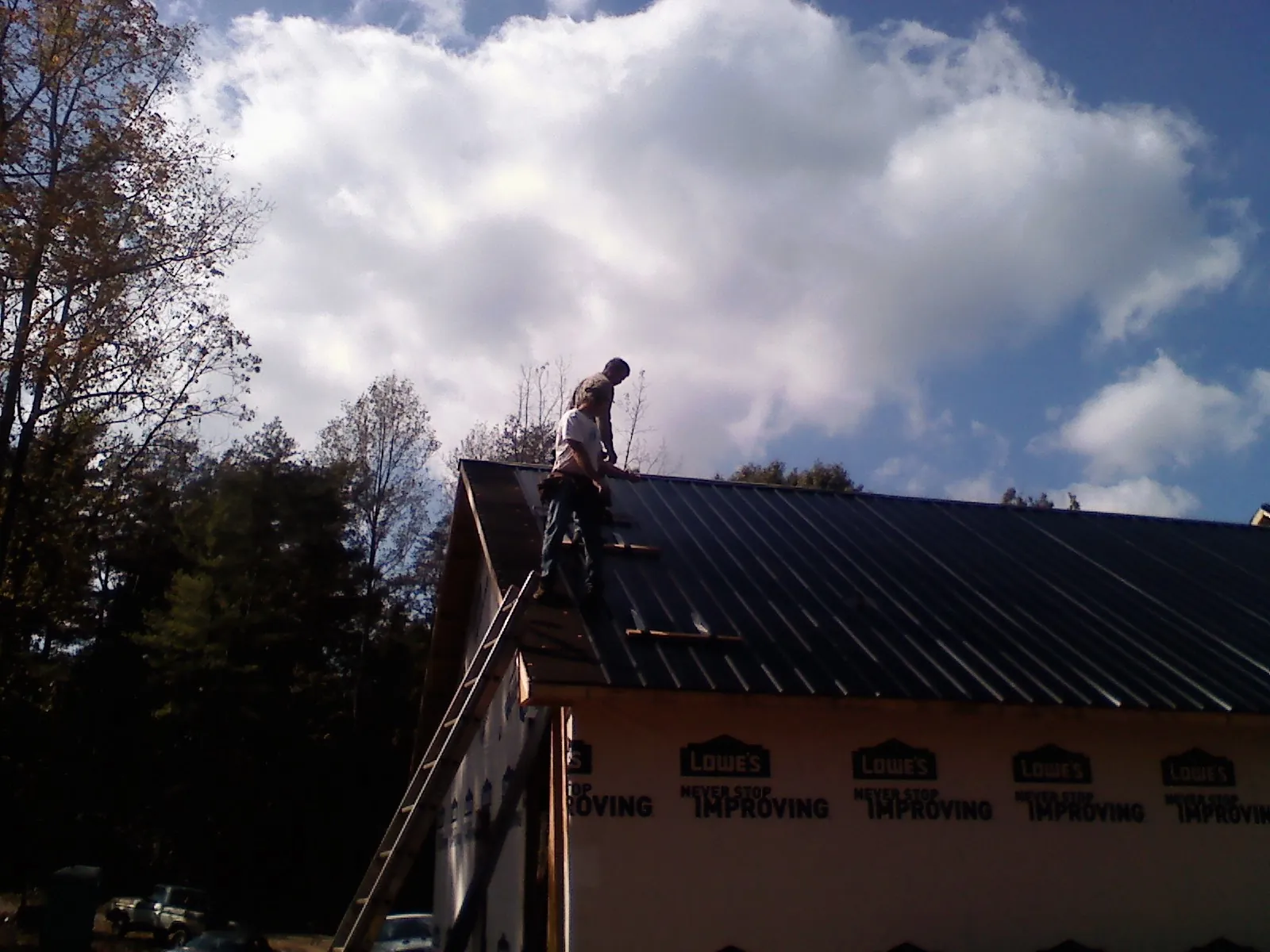 Roofer fastening dark metal panels high against a cloudy sky, from a Roof Inspection job in Manitou