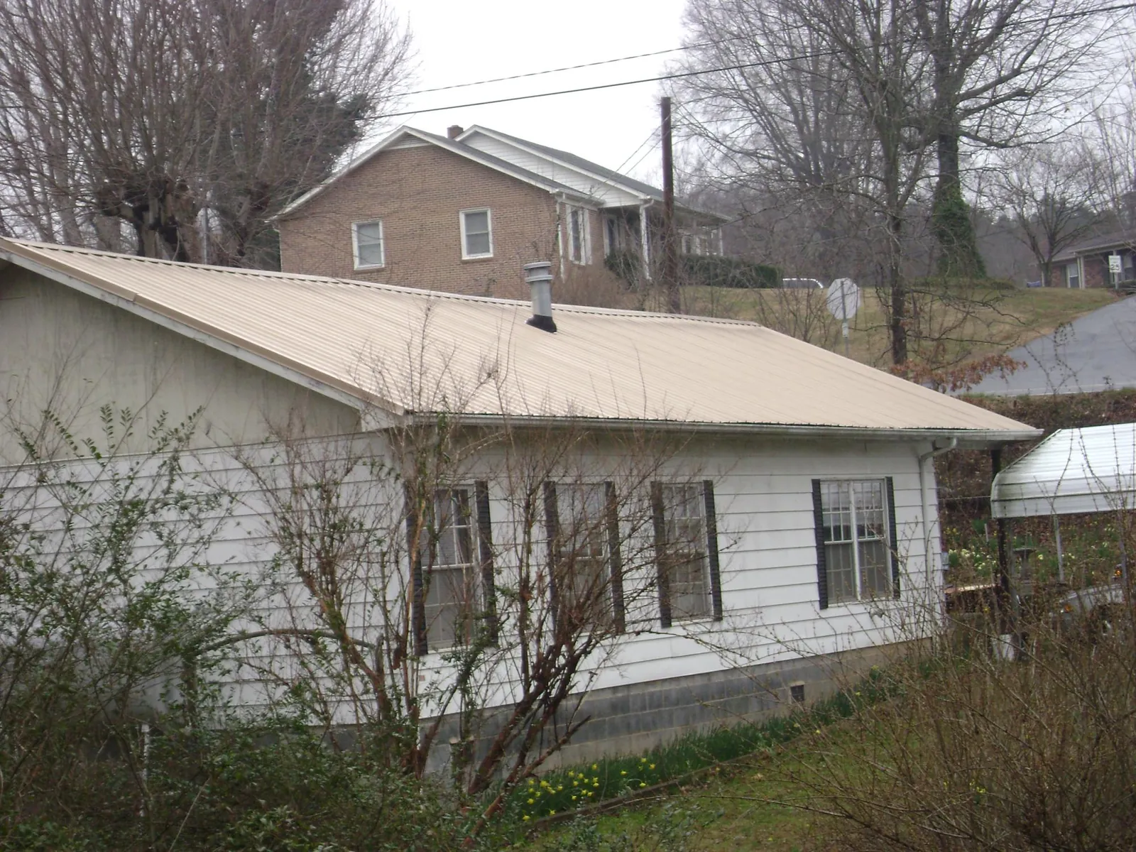 Tan metal roof on a white sided house set into a hillside — Commercial Roofing by Roofing Brothers in Manitou