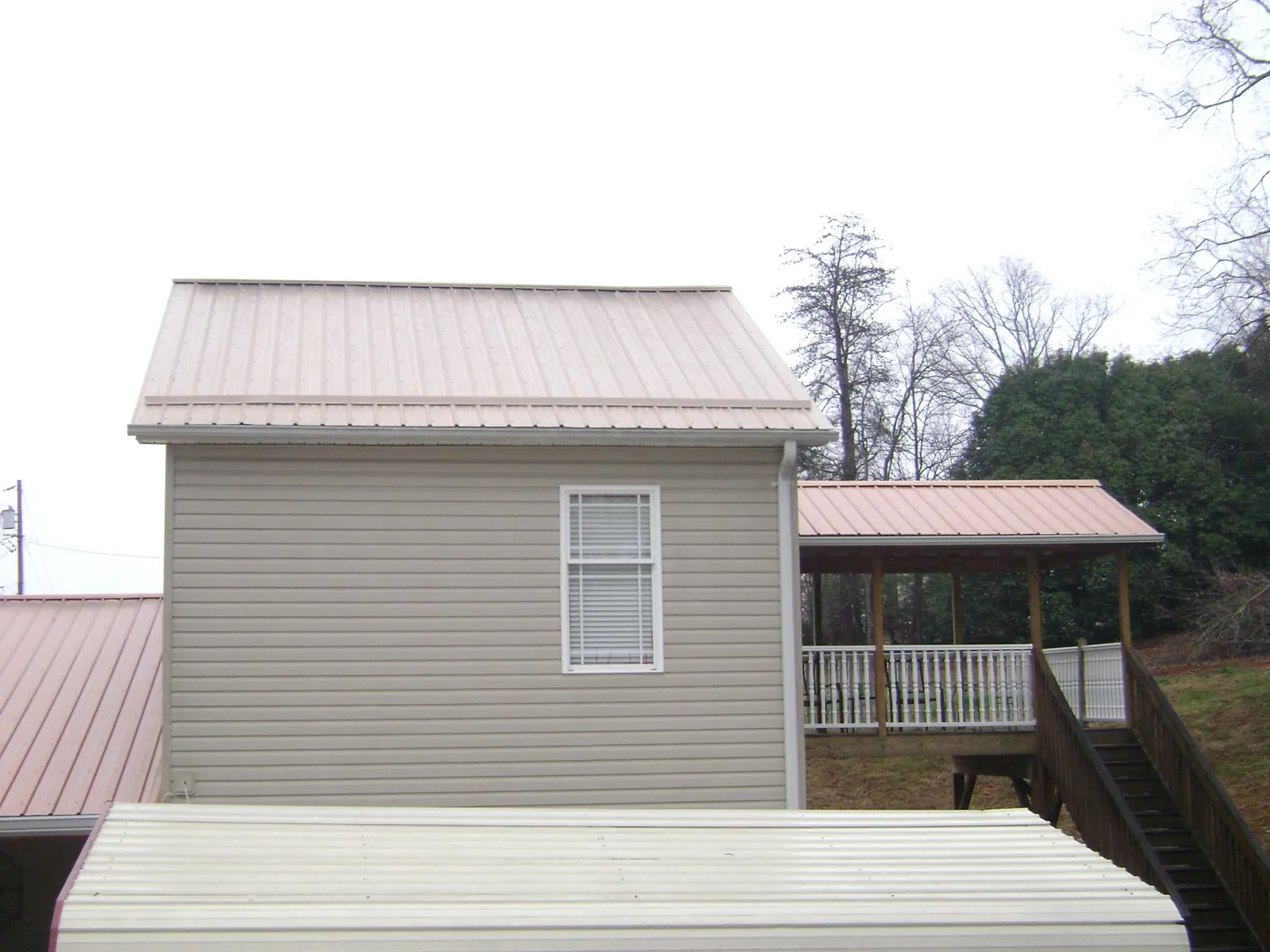 Tan metal roofs on a two story addition and attached porch, from a Roof Replacement job in Manitou